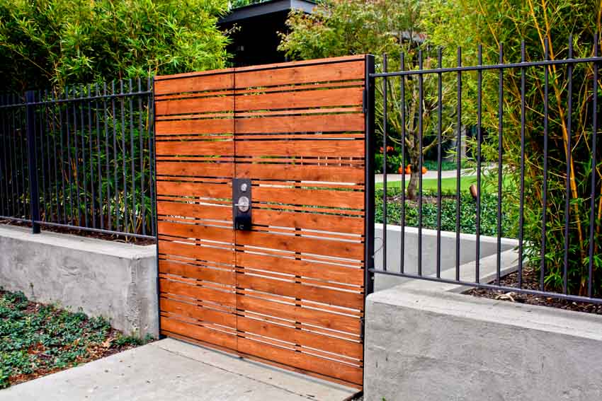 Black lock on a wood gate, wrought iron fence and concrete walkway