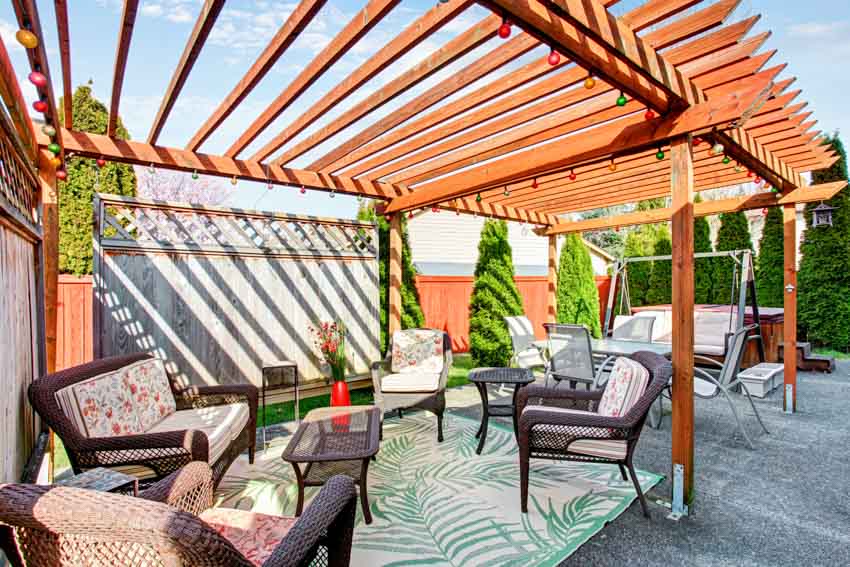 Outdoor area with pergola privacy panel, concrete flooring, cushioned chairs, small table, rug, and hedge trees