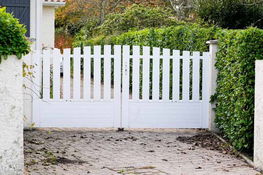 Outdoor driveway with vinyl fence and hedge plants