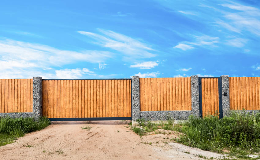 Fence made of vertical wood plats and sandy driveway