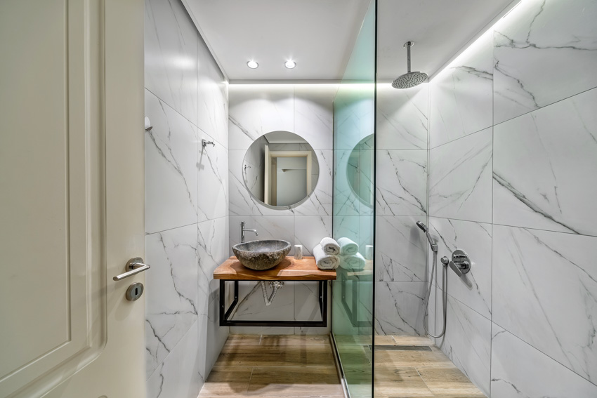 Small bathroom with large format tile, shower, glass divider, mirror, countertop, floating vanity, and door