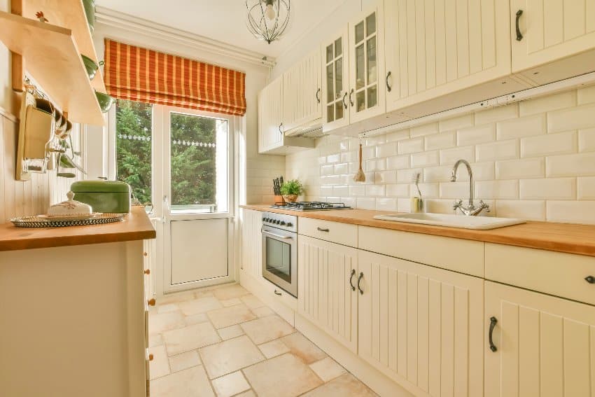 Small kitchen interior in white tones with wooden countertops, grooved kitchen cabinets, furniture and tiled floors 