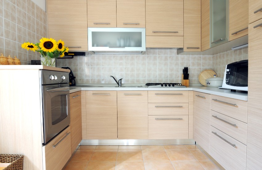A small kitchen with white oak shaker cabinets, sunflower display on top of oven, tiled backsplash and flooring