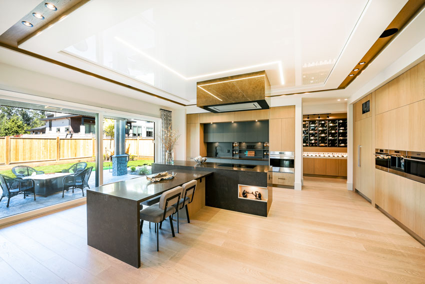 Spacious kitchen with peninsula, chairs, wine storage, windows, range hood, backsplash, and wood floors