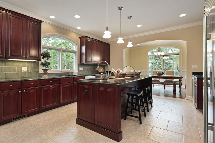 Spacious kitchen with tile floors, center island, mahogany cabinets, chairs, backsplash, hanging lights, and windows