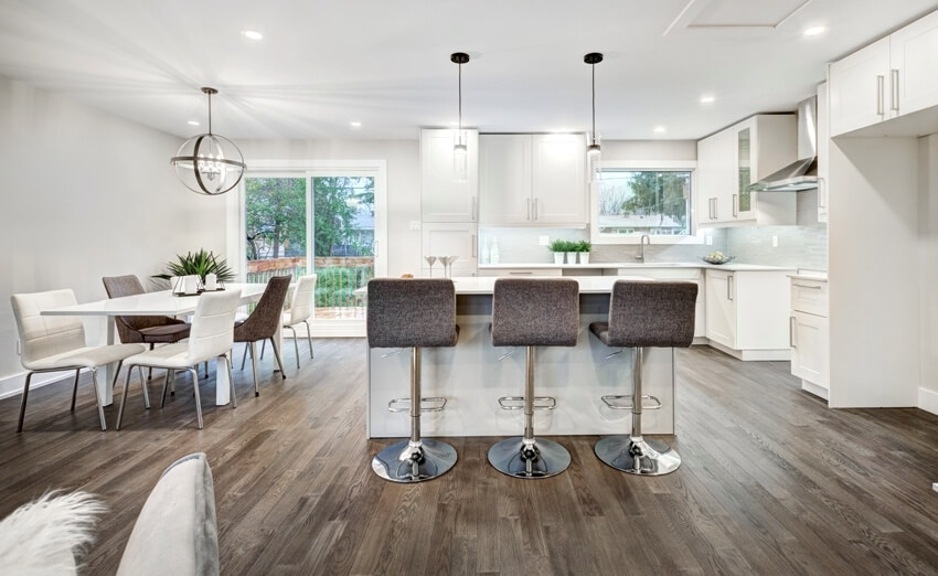 Spacious white kitchen with dining set, pendant lights, island with chairs and linoleum flooring