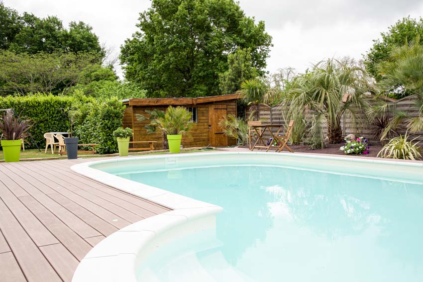 Swimming pool with traditional white plaster, wood deck fence, potted plants, and shed