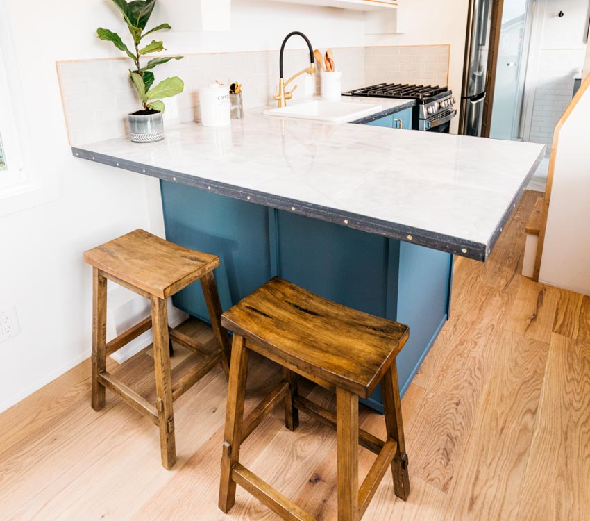 Tiny house kitchen with peninsula seating, bar stools, wood floor, sink, countertop, backsplash, and indoor plant