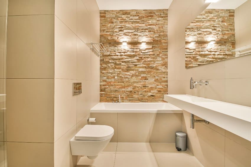 White tiled bathroom interior with stone accent wall, a bathtub and toilet