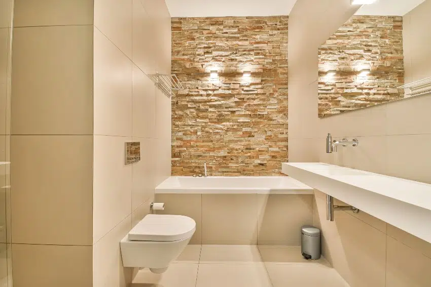 White tiled bathroom interior with stone accent wall, a bathtub and toilet
