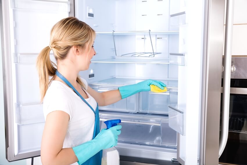 A woman cleaning empty refrigerator in kitchen
