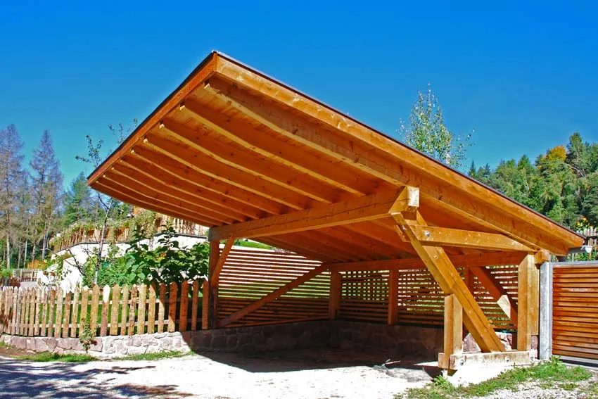 Wood carport with sloped roof, and stone driveway