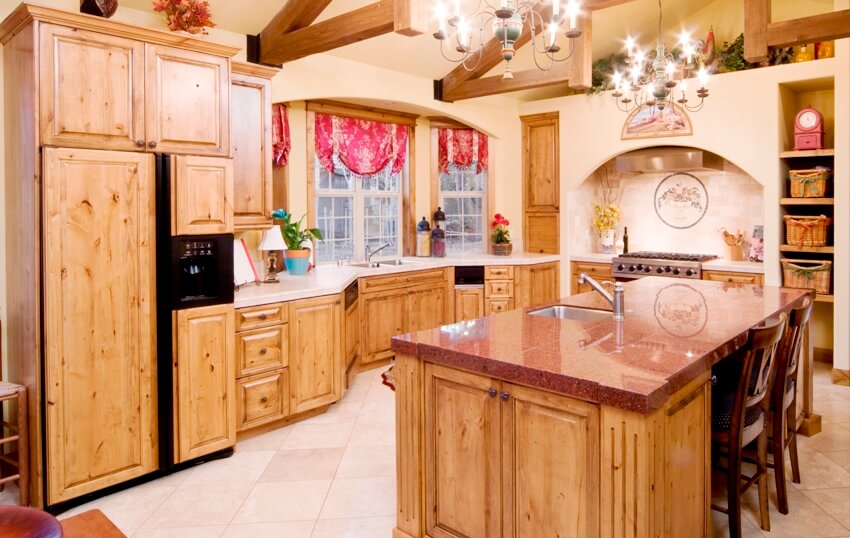 Rustic kitchen interior with wood beams on ceiling, kitchen island with red granite counter and knotty alder cabinets