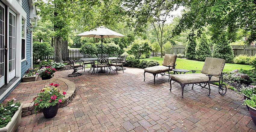 Backyard with brick pavers flooring patio table with umbrella lounge chairs