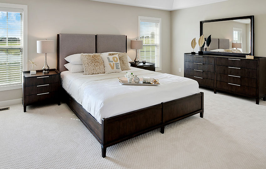 Bedroom with carpeted floor, bed with wood frame and table with lampshade 