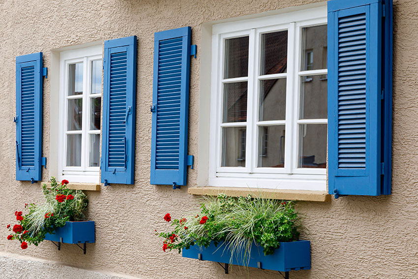 Stucco house wall with French windows with shutters and flower box
