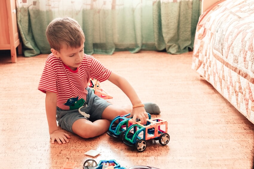 A boy plays with magnetic constructor in kids room with cork flooring