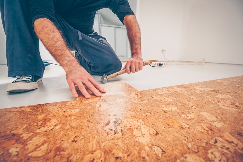 A man layering cork flooring with a hammer