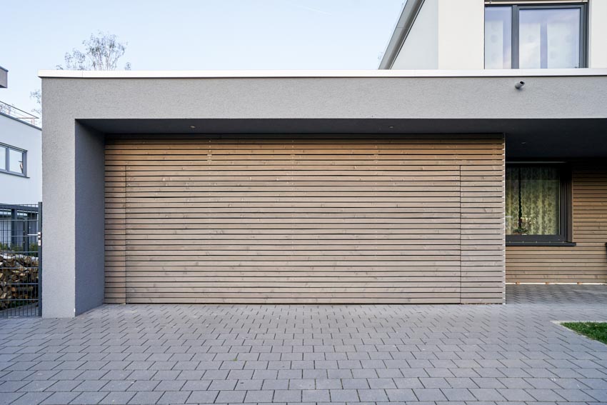 Attached garage with paver driveway, flat roof, and louvered garage doors