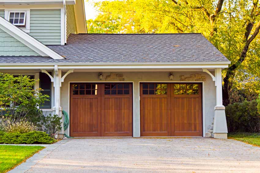 Attached garage with shingle roof, driveway, and wood farmhouse garage doors