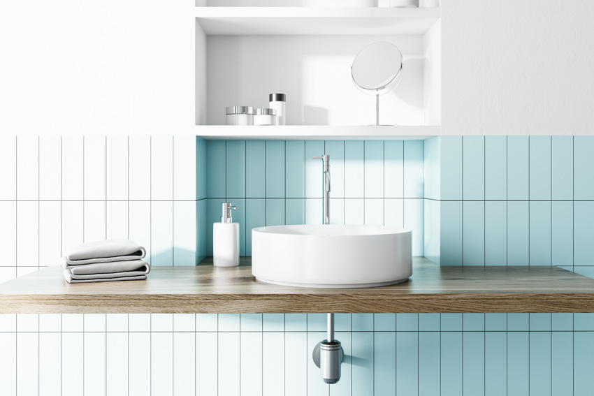 Bathroom vanity with kit kat tile backsplash, floating wood countertop, sink, and bathroom essentials