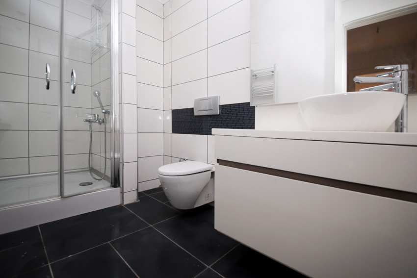 Bathroom with black alternating size floor tiles, vanity, toilet, shower, glass door, faucet, and mirror