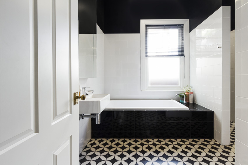 Bathroom with pattern style black and white ceramic tiles, tub, window, sink, and mirror