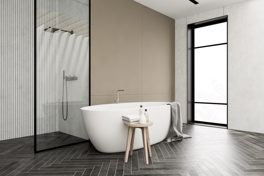 Bathroom with black herringbone tile floors, tub, stool, shower, glass divider, and window