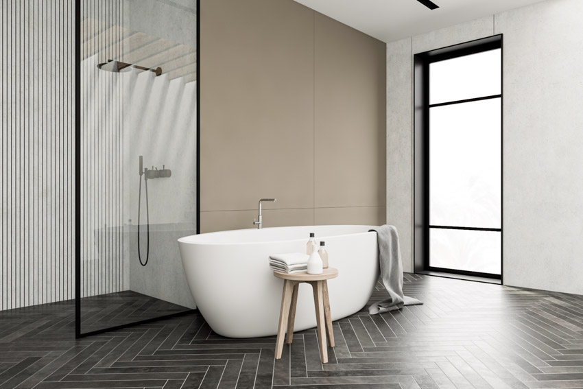 Bathroom with herringbone tile in black, tub, stool, shower, glass enclosure, and window