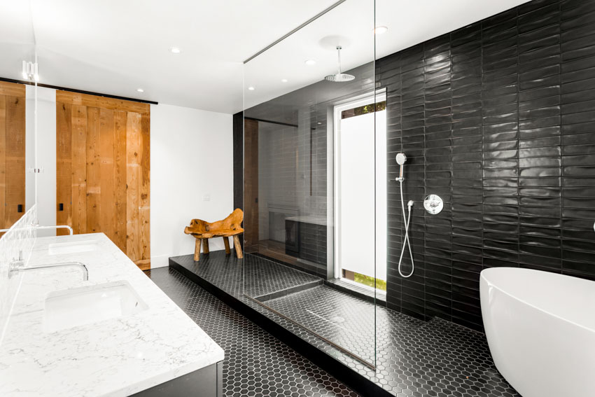 Bathroom with black hexagon floor tiles, shower, tub, glass divider, window, sink, countertop, and wood door