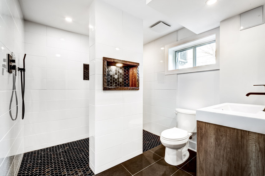 Bathroom with penny tile flooring, white tile walls, shower, toilet, sink, and window