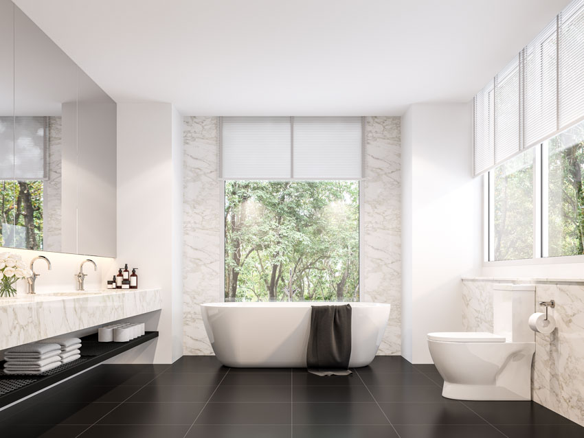 Bathroom with black tile floor, tub, windows, roman shades, toilet, vanity area, faucets, and mirror