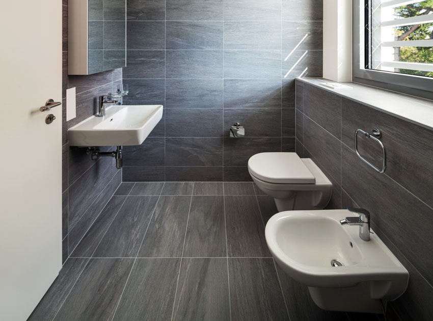 Bathroom with black stone look vinyl floor tiles, toilet, bidet, jalousie, windows, sink, faucet, and mirror