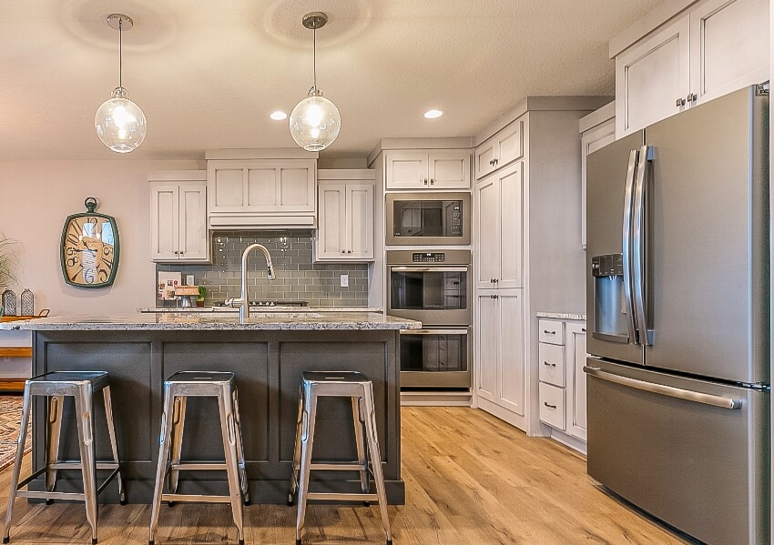 Beautiful kitchen with wood floors, grey island with stools, large fridge and standard triple wall ovens, subway backsplash and pull down faucet