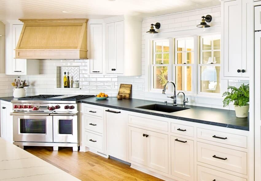 A beautiful white kitchen with wood flooring, stainless steel stove and wall sconces