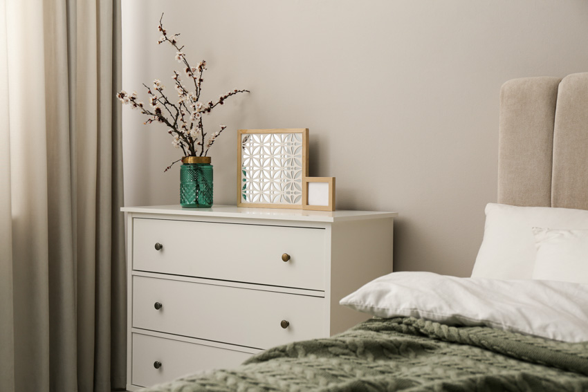 Bedroom with comforter, curtain, and dresser as creative nightstand alternative