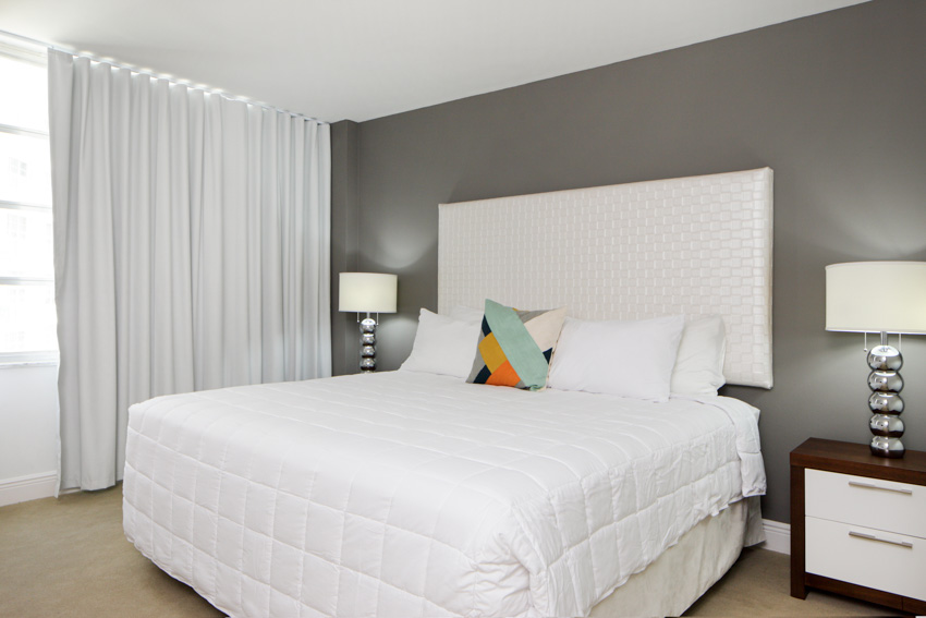 Bedroom with cotton type of curtain fabric, headboard, comforter, nightstands, pillows, and lamps