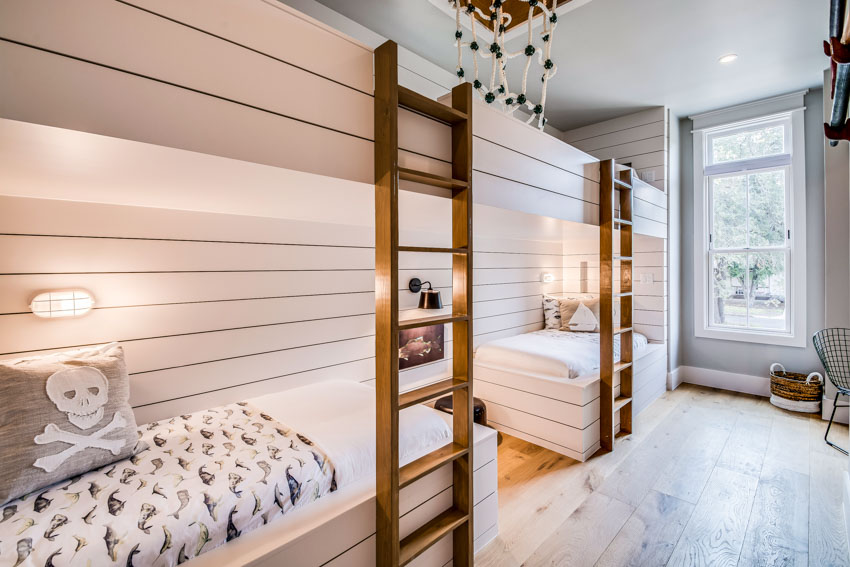 Bedroom with long bunk beds, ladders, mattresses, pillows, wall-mounted lights, and windows