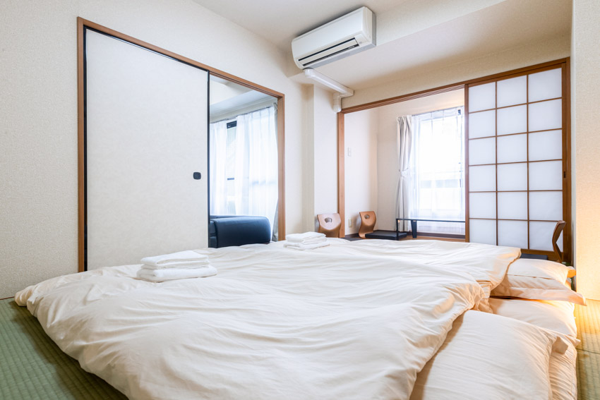 Bedroom with padded Japanese floor mattress, air conditioner, and sliding door