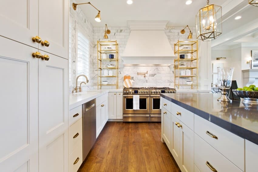Bright contemporary kitchen with white cabinets, wood floors, stainless steel appliances, and gold brass wall sconces and accents