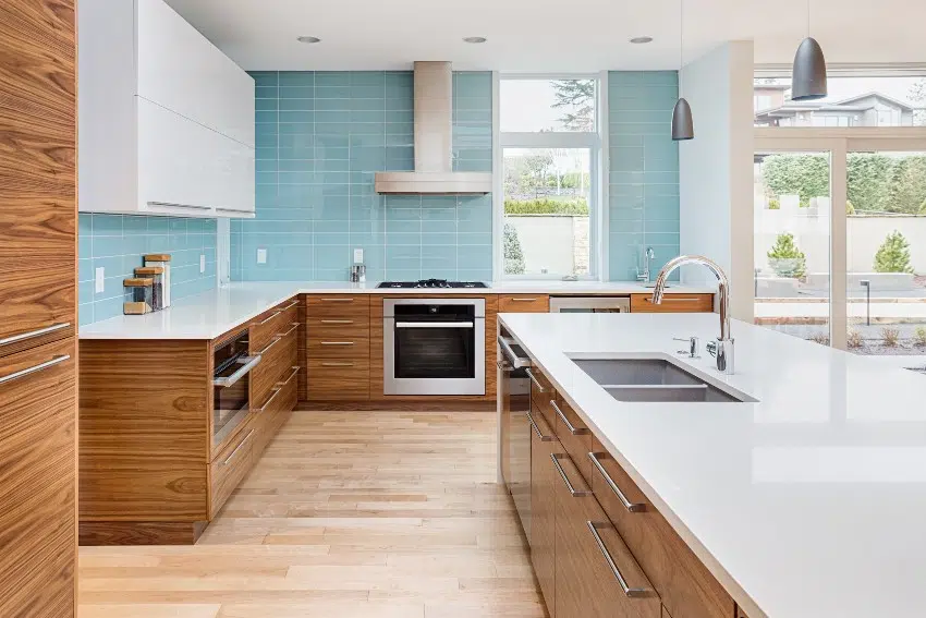 Bright and fresh looking kitchen with wooden cabinets, island with sink, pendant lights and sky blue frosted glass backsplash