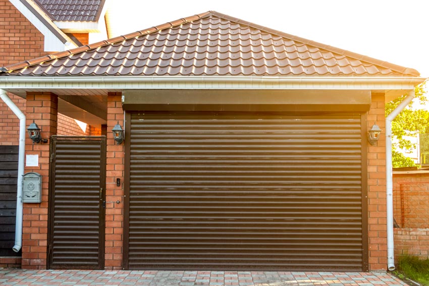 Detached garage with louvered garage doors, pitched shingle roof, and lighting fixtures