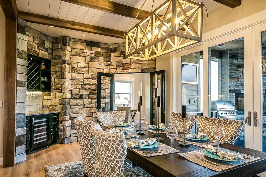 Dining area with stone walls, chandelier, table, chairs, candle centerpiece, wooden floor and windows