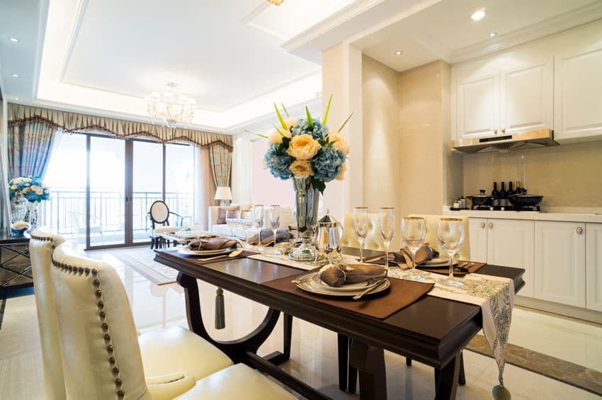 Dining room with table, chairs, centerpiece, plates, glasses, dry bar, cabinets, backsplash, window, and curtains