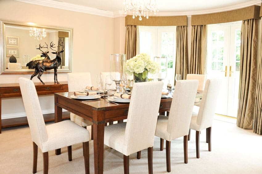 Dining room with table, chairs, vase centerpiece, flowers, console table, mirror, window, and curtains