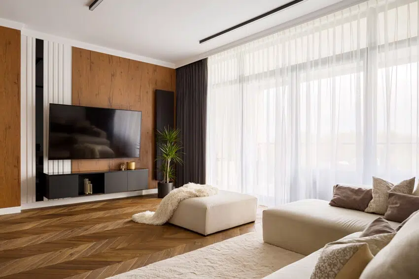 Elegant designed living room with window wall and double layered sheer curtains, big television screen and wooden elements