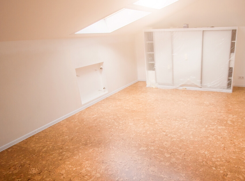 An empty attic with cork flooring, white walls and cabinets