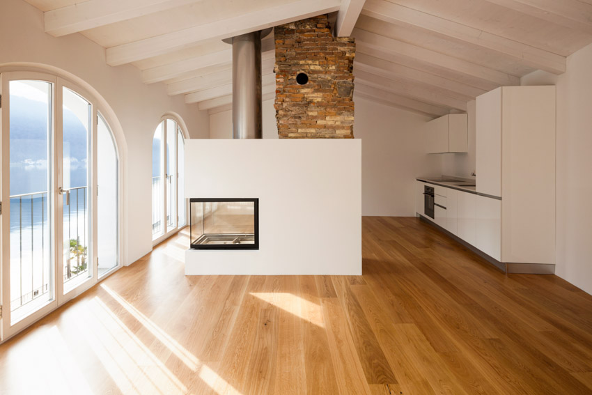 Empty room with natural red oak floors, fireplace, white walls, and windows