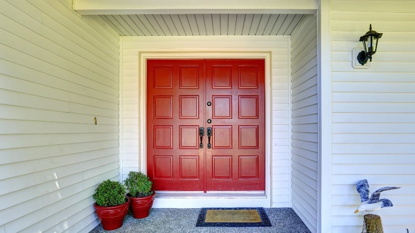 Entrance porch with horizontal shiplap walls and red door decorated with flower pots