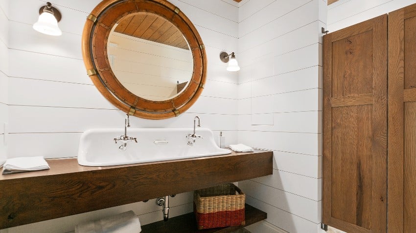 A farmhouse bathroom interior with round mirror and sconce lights on a shiplap wall